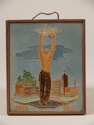 Herdenkingstegel met decor van man met zwaan voor fabriekscomplex en tekst 1926-1951