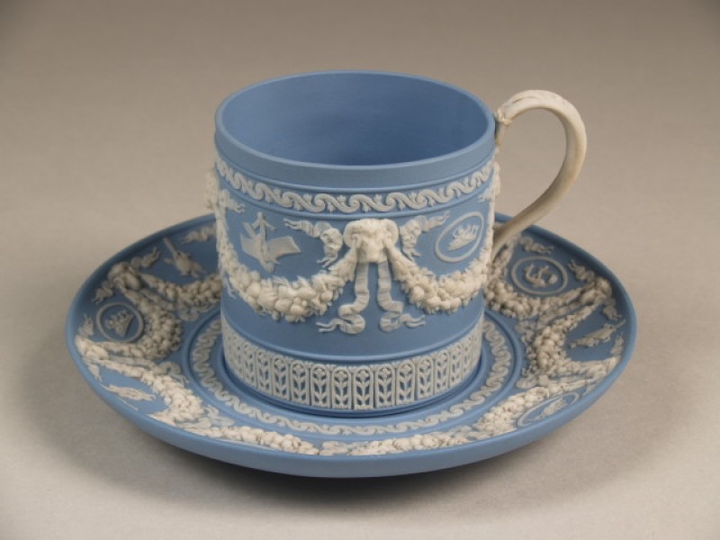 Kop en schotel met in reliëf witte guirlandes op blauw fond; jasperware