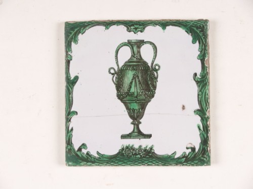 Tegel met een groenzwart decor van een vaas in een florale omlijsting